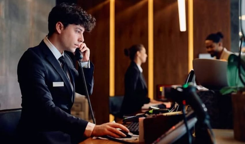 Young,Receptionist,Making,A,Phone,Call,While,Working,On,Desktop