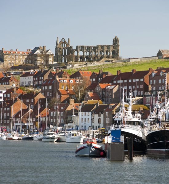 View of small fishing boats moored in the Whitby upper harbour with the ruins of Whitby Abbey visible on the skyline behind